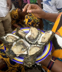 In a circled of onlookers, a woman holds a plate of shucked oysters.